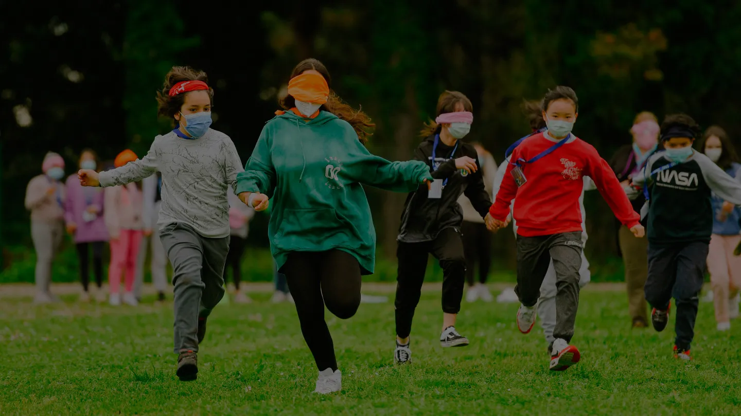 Nenos, nenas e mozos correndo xuntos ao aire libre como parte dunha actividade de Enki.