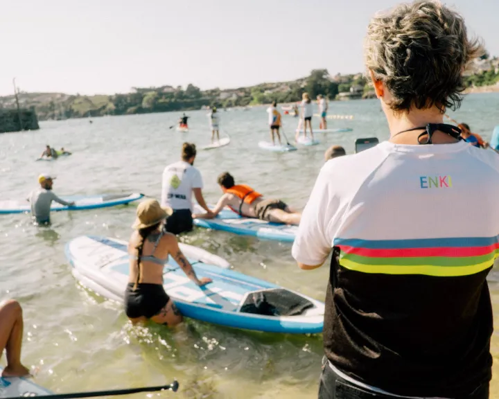 Persoas de pé en augas pouco profundas con táboas de paddle surf durante unha actividade de Enki.