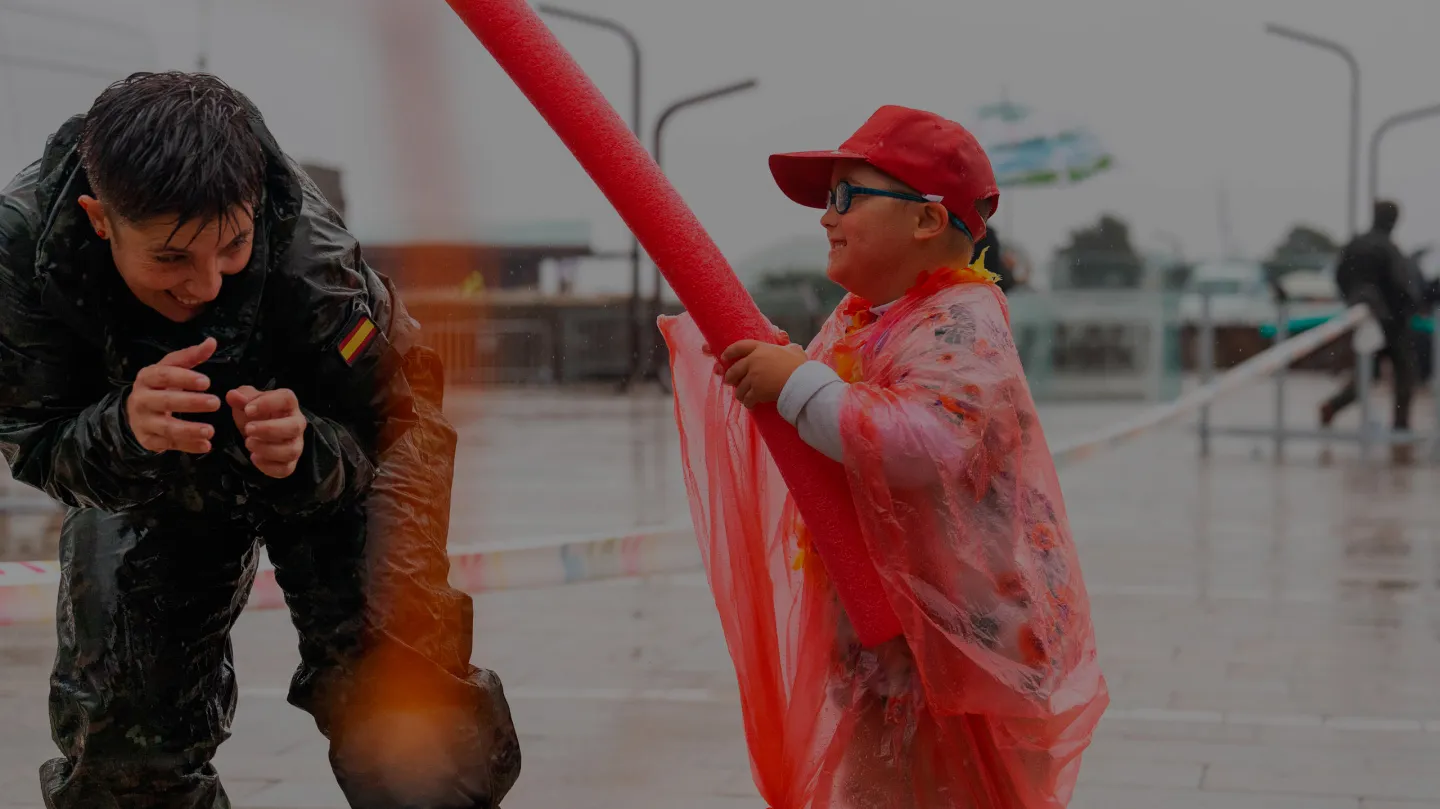 Un neno e unha persoa adulta compartindo un momento lúdico ao aire libre baixo a choiva durante unha actividade de Enki.